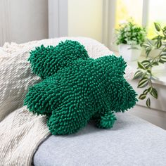 a green stuffed animal sitting on top of a couch next to a potted plant