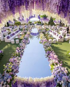 an outdoor ceremony setup with purple flowers and white couches on the grass, surrounded by greenery