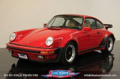 a red porsche sits on a black surface in a white walled room with reflective flooring