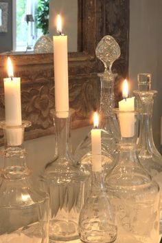 a table topped with lots of glass vases filled with candles next to a mirror