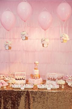 a table topped with lots of cakes and desserts next to pink balloons on the wall