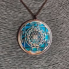 "Sri Yantra in rose gold on 925 silver and acquamarine mother of pearl. It's one of the most powerful symbol in sacred geometry, belonging both to Induism and Buddhism traditions. It has a complex structure made of nine interlocking triangles: four of them, looking upside, show male power and Shiva, five of them, looking down side, express a female Energy and her Goddes Shakti. These 43 triangles represent the cosmos and the human body, they surround a point known as bindu, source of Creation. T Luxury Spiritual Jewelry For Navratri, Spiritual Hallmarked Necklaces, Symbolic Turquoise Necklace For Gift, Blue Gemstone Symbolic Necklace, Blue Hallmarked Spiritual Necklaces, Blue Spiritual Locket Jewelry, Complex Structure, Luck Symbols, Sacred Geometry Jewelry