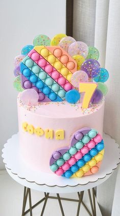 a pink cake with colorful decorations on top sitting on a white table next to a window