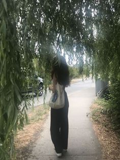 a woman walking down a sidewalk next to trees