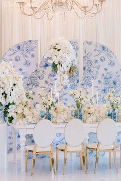 a dining room table with blue and white china on the wall behind it, surrounded by floral centerpieces