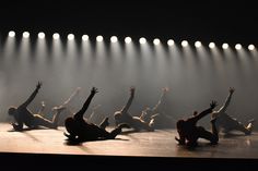 dancers on stage with their arms in the air and lights shining down from behind them