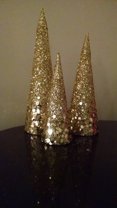 three small gold glitter trees on a black table