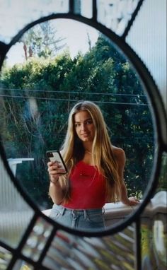 a woman is looking at her cell phone in the mirror while standing on a porch