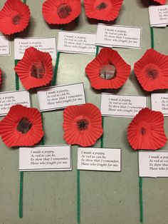 red paper flowers are arranged in rows on a table with cards attached to the stems