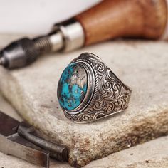 Immerse yourself in the beauty of authentic craftsmanship with our handcrafted silver ring, enriched with a genuine turquoise stone and adorned with traditional motifs. The oval mount harmoniously embraces the turquoise, creating a centerpiece that is both captivating and meaningful. Every detail of this ring tells a story of tradition, enhancing its charm and making it a treasure in your jewelry collection. It's more than a ring; it's a celebration of artistry and the natural beauty of turquois Southwestern Style Engraved Turquoise Ring As Gift, Engraved Southwestern Style Turquoise Ring For Gift, Artisan Turquoise Ring, Engraved Turquoise Rings As Gift, Artisan Turquoise Inlay Ring As A Gift, Artisan Turquoise Inlay Ring As Gift, Artisan Turquoise Inlay Ring For Gift, Traditional Sterling Silver Turquoise Ring, Traditional Sterling Silver Turquoise Gemstone Ring