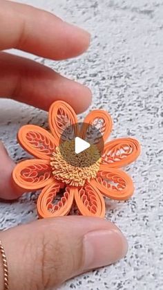 someone is holding an orange flower brooch in their left hand, with the video below it