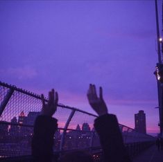 two people are standing on a bridge with their hands up in the air at dusk