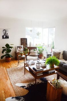 a living room filled with lots of furniture and plants on top of wooden flooring