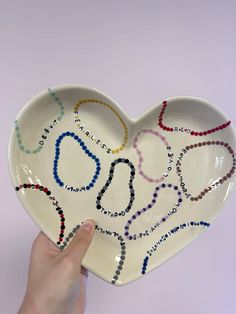 a hand holding a heart shaped plate with beads on it