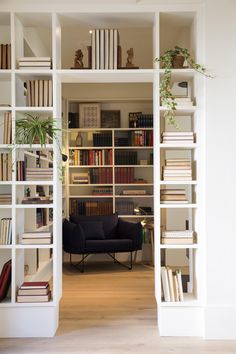 an open book shelf filled with books next to a black chair and potted plant