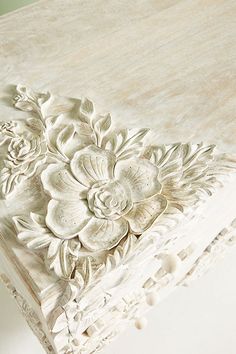 a close up of a white table with flowers and leaves on the top, as if it were carved from wood