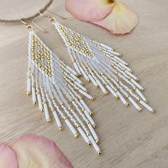 white and gold beaded earrings on a wooden table next to pink flower with petals