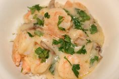 a white bowl filled with shrimp and rice covered in sauce, garnished with parsley