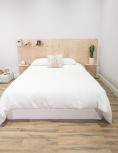 a bed with white sheets and pillows on top of wooden flooring in a room