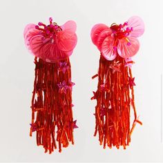 two pairs of pink and red earrings with flowers on them, hanging from strings in front of a white background