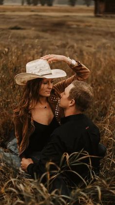 a man and woman are sitting in the middle of a field with a hat on their head