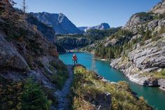 a person standing on the edge of a cliff overlooking a lake and mountains in the distance