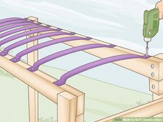 a hand holding a drill over a wooden structure with purple straps on it and a green object in the background