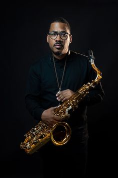 a man is holding a saxophone in his right hand and posing for the camera on a black background