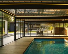 an indoor swimming pool surrounded by glass walls and wood flooring, with sliding doors leading to the patio area