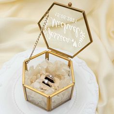 an open glass box with wedding rings inside on a white plate and gold chain around it