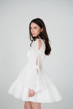 This short wedding dress features a satin bodice with boning and lacing on the back. The skirt with ruffle detailing, and long sleeves adorned with cute bows. Perfect as a second wedding dress or bridal shower dress. Short Embroidered Dress, Vintage Short Wedding Dress Retro, Short Wedding Dress Long Sleeves, Elopement Dress Long Sleeve, Short Dress With Jacket, Casual Wedding Dress Backyard, Engagement Dresses Elegant, Reception Dresses For Bride, Short Elopement Dress