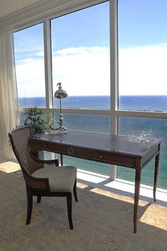 a desk and chair in front of large windows overlooking the ocean