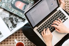 a woman is typing on her laptop while holding a cup of coffee and reading books