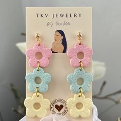 two pairs of earrings with flowers on them sitting in front of a card and flower bouquet