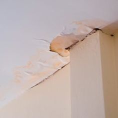 the corner of a white wall with peeling paint on it's walls and ceiling