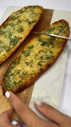 two pieces of bread with cheese and spinach on it being cut by a knife