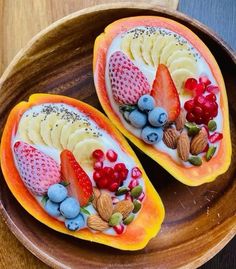 two pieces of fruit with nuts and berries on them sitting in a wooden bowl next to each other