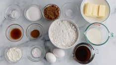 an assortment of ingredients are shown in bowls on a marble countertop, including butter, eggs, flour, and sugar