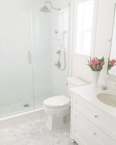 a white bathroom with pink flowers in the vase on the sink and shower stall door