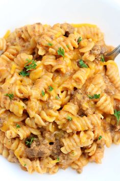 a white plate topped with macaroni and cheese covered in meat, parsley