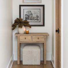 a small wooden table with a vase and candle on it next to a white bench