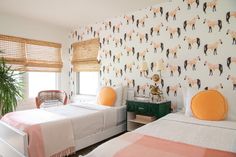 two beds in a room with wallpaper and orange pillows