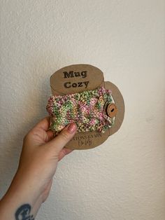 a person holding up a small wallet in front of a wall with the words mug cozy on it