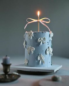 a blue cake sitting on top of a table with a lit candle in the middle