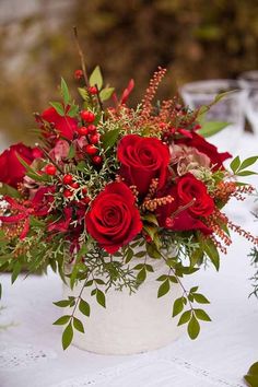 a white vase filled with red roses on top of a table covered in greenery