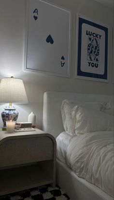 a white bed sitting next to a night stand with two framed pictures on the wall