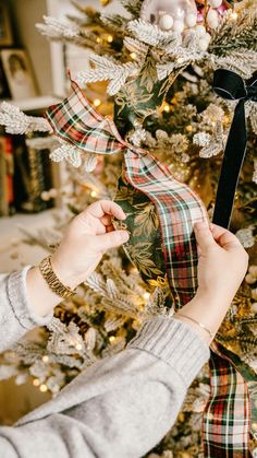 a woman is decorating a christmas tree with black and white ribbon on the top