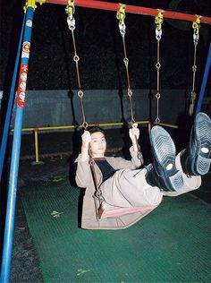 a woman sitting on a swing with her feet hanging off the ground and holding onto it