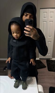 a man in a black hoodie taking a selfie with his little child on the phone