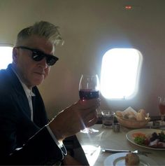 a man sitting at a table with a glass of wine in his hand and food on the plate next to him